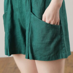 May include: Emerald green linen shorts with large front pockets. The shorts have a relaxed fit and a button closure. The fabric appears to be lightweight and breathable, suitable for warm weather. The shorts are a solid color.