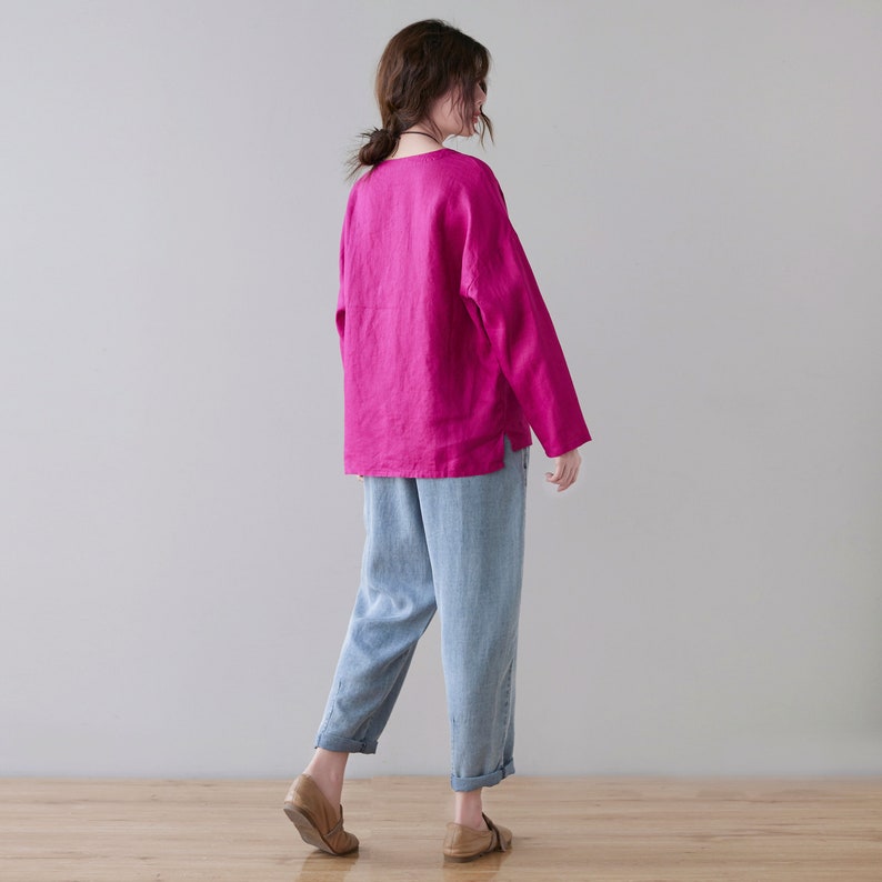May include: A woman wearing a long-sleeved magenta top and light blue pants. The top has a simple neckline and a relaxed fit. The pants are cuffed at the ankles. The outfit is completed with brown shoes.