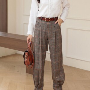 K&ouml;nnte beinhalten: Ein Outfit f&uuml;r Damen mit einem wei&szlig;en Hemd mit Kn&ouml;pfen, einer braunen karierten Hose und einem braunen Lederg&uuml;rtel mit goldener Schnalle. Das Outfit wird durch eine braune Lederhandtasche und braune Stiefeletten erg&auml;nzt.