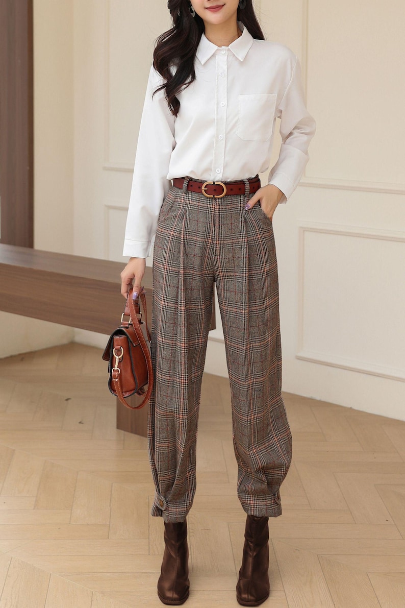 K&ouml;nnte beinhalten: Ein Outfit f&uuml;r Damen mit einem wei&szlig;en Hemd mit Kn&ouml;pfen, einer braunen karierten Hose und einem braunen Lederg&uuml;rtel mit goldener Schnalle. Das Outfit wird durch eine braune Lederhandtasche und braune Stiefeletten erg&auml;nzt.