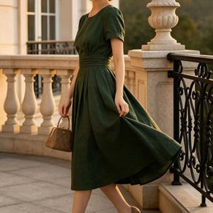 May include: A dark green midi dress with short sleeves, a round neckline, and a pleated skirt. The outfit includes a wide-brimmed straw hat, a small brown structured handbag with a metal clasp, and two-tone brown and black pointed-toe heels.