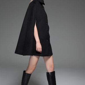 May include: A black cape with a high collar and button fastening. The cape is made from a soft, warm fabric and has a flowing silhouette. The model is wearing black knee-high boots.