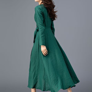 May include: A long-sleeved, emerald green dress with a wrap-style bodice and a flowing skirt. The dress has a tie belt at the waist and is made of a lightweight fabric.