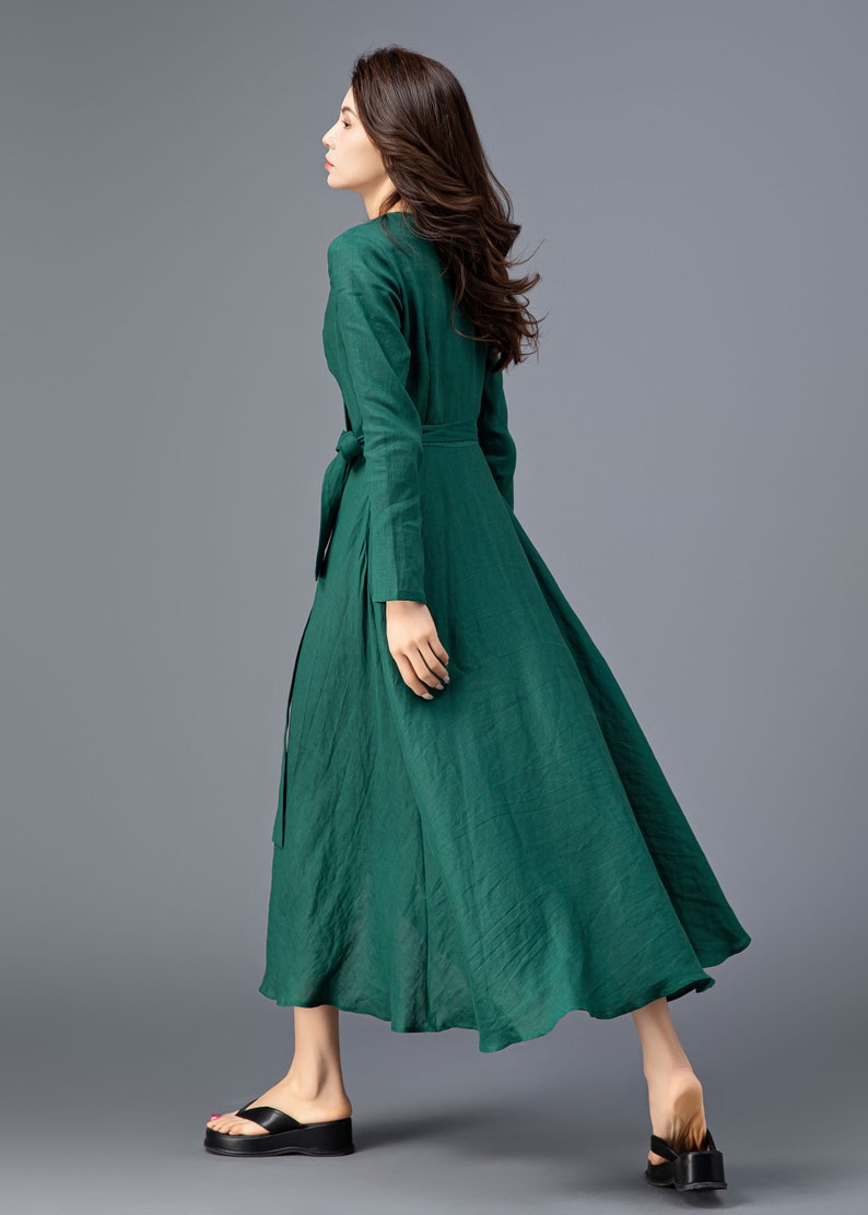 May include: A long-sleeved, emerald green dress with a wrap-style bodice and a flowing skirt. The dress has a tie belt at the waist and is made of a lightweight fabric.
