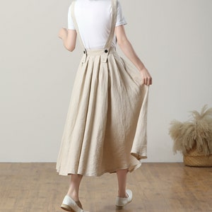 May include: A beige linen midi skirt with adjustable straps and a pleated design. The skirt has a relaxed fit and is perfect for a casual summer look.