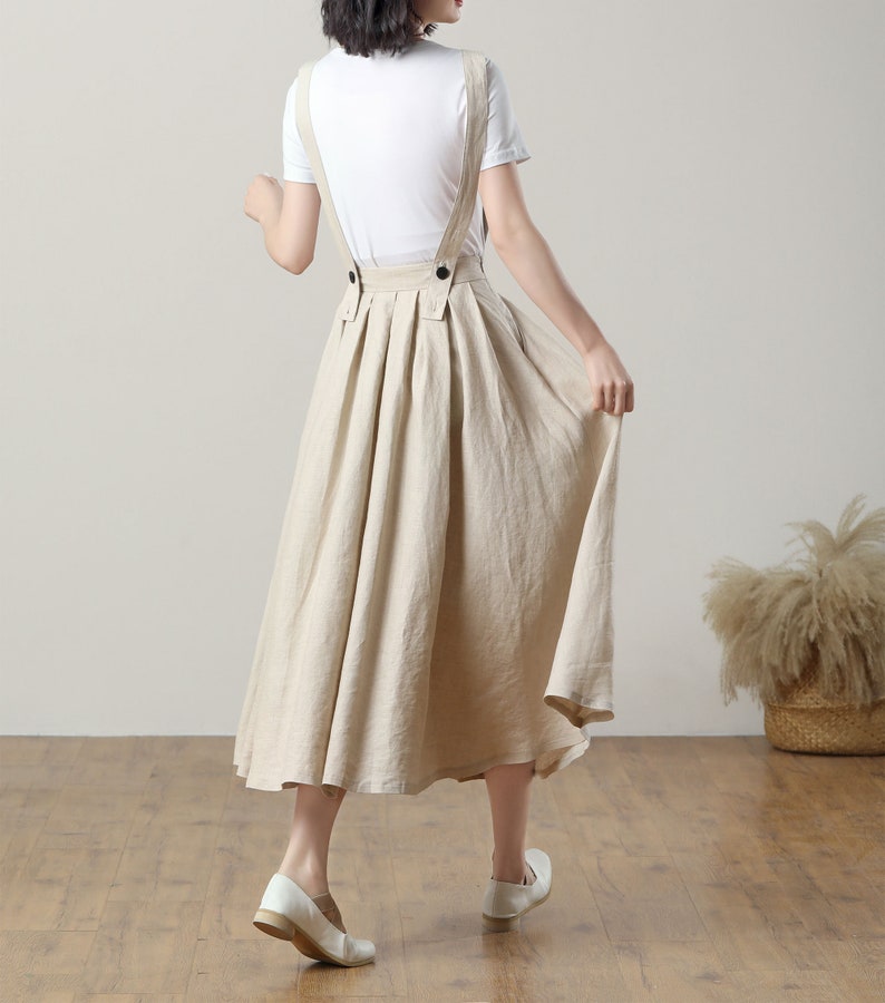 May include: A beige linen midi skirt with adjustable straps and a pleated design. The skirt has a relaxed fit and is perfect for a casual summer look.