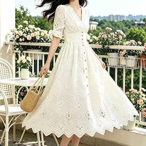 Puede incluir: Vestido blanco de ojal con cuello en V, mangas cortas y botones delanteros. El vestido presenta una cintura entallada y una falda fluida con dobladillo festoneado. Se sostiene un bolso de mano de paja tejida. Adecuado para un día de verano.