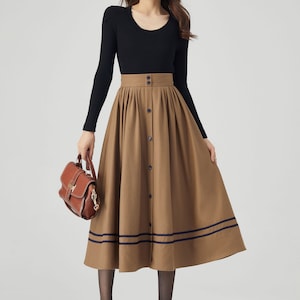 May include: A brown midi skirt with a button-up front and two navy blue stripes at the hem. The skirt is pleated and has a high waist.