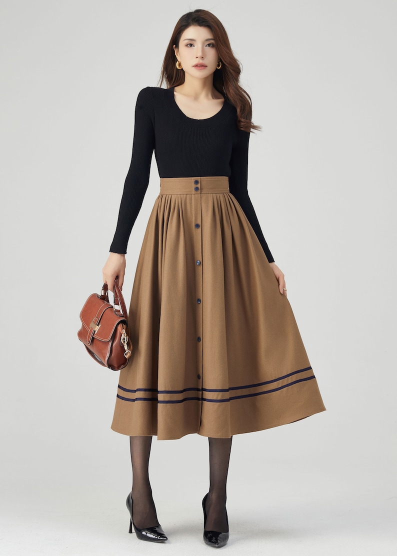 May include: A brown midi skirt with a button-up front and two navy blue stripes at the hem. The skirt is pleated and has a high waist.