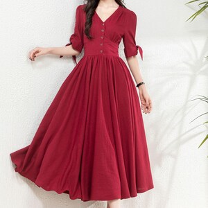 May include: A red midi dress with a v-neckline, button-up front, and short sleeves with ties. The dress has a fitted bodice and a full skirt.