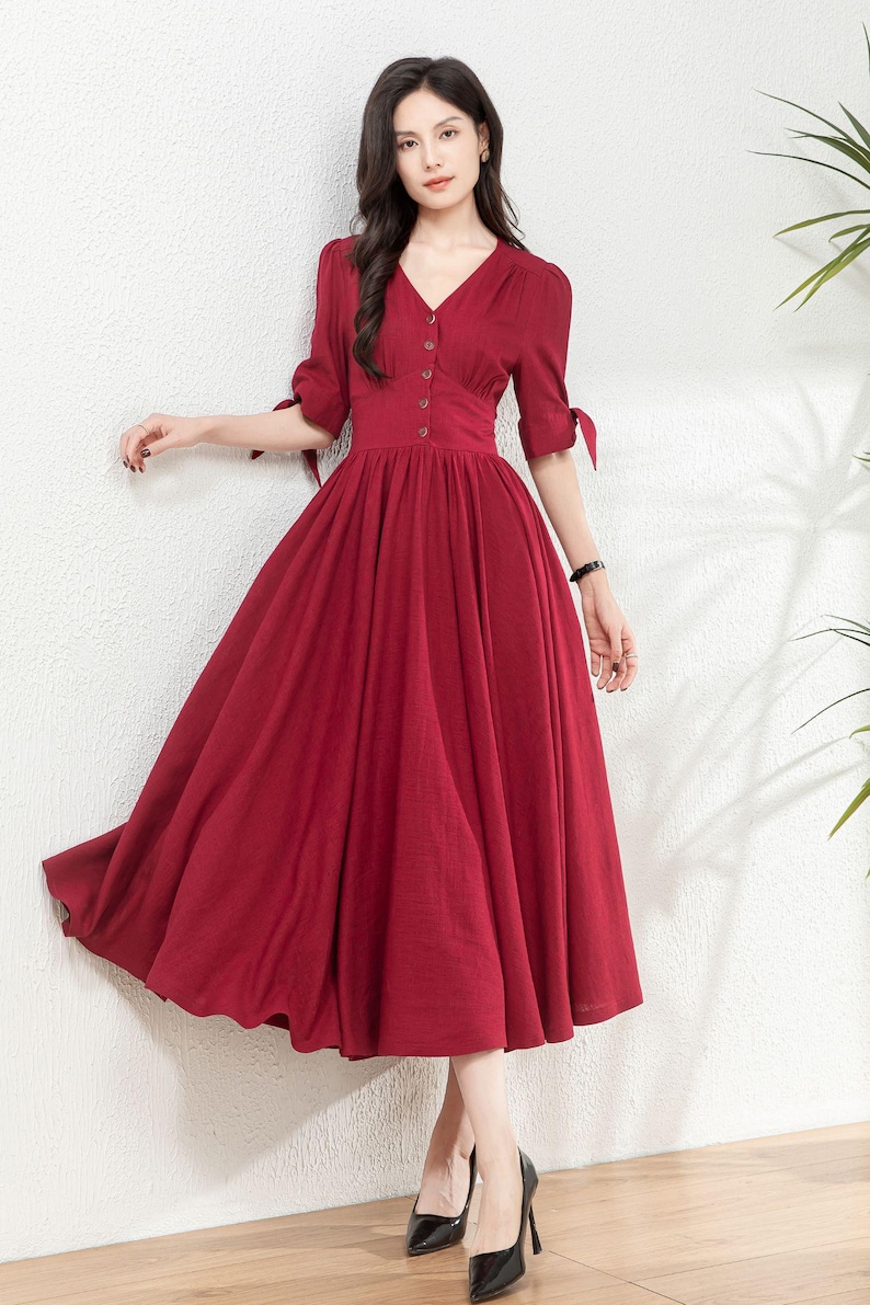 May include: A red midi dress with a v-neckline, button-up front, and short sleeves with ties. The dress has a fitted bodice and a full skirt.