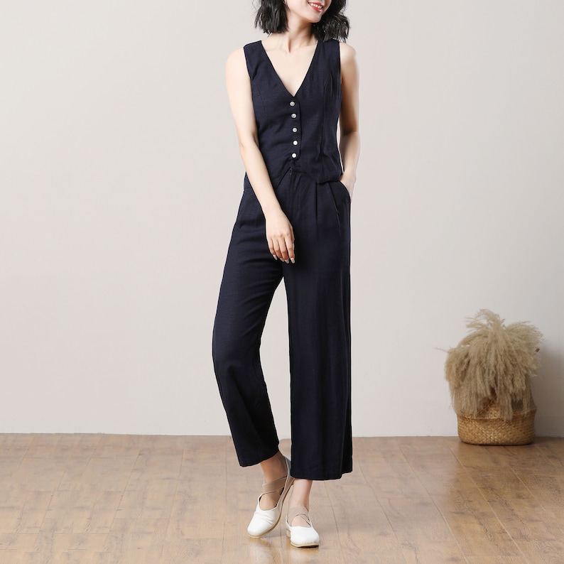 May include: A navy blue sleeveless jumpsuit with a button-up front and wide-leg trousers. The jumpsuit is made of a lightweight fabric and has a relaxed fit.
