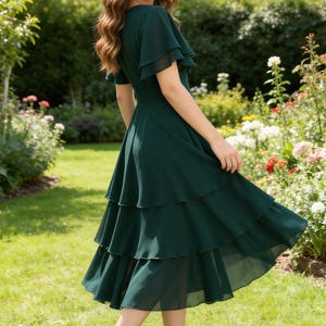 May include: A dark green, tiered midi dress with flutter sleeves. The dress is made of a flowing fabric and is paired with black heeled sandals. The background features a garden with green grass and colorful flowers.