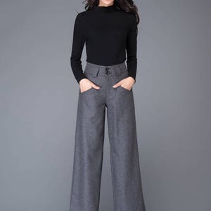 Puede incluir: Una mujer con un su&eacute;ter negro de cuello alto y pantalones grises de pierna ancha con cintura alta y bolsillos. Lleva tacones negros.