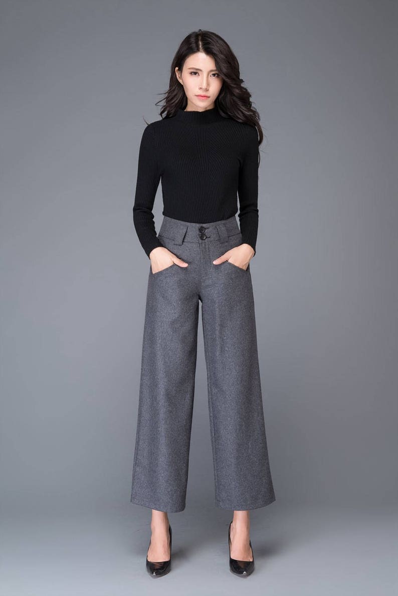 Puede incluir: Una mujer con un su&eacute;ter negro de cuello alto y pantalones grises de pierna ancha con cintura alta y bolsillos. Lleva tacones negros.