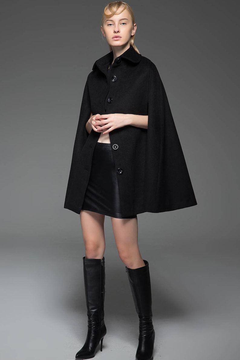 May include: A black wool cape with a collar and button fastening. The cape is worn over a black skirt and black knee-high boots.