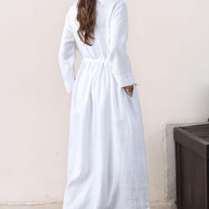 May include: A white long-sleeved linen dress with a drawstring waist and pockets. The dress is flowy and has a relaxed fit.
