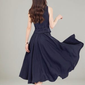 Peut inclure: Une robe bleu marine sans manches avec une jupe qui s'&eacute;vase &agrave; partir de la taille. La robe a une fermeture boutonn&eacute;e dans le dos.