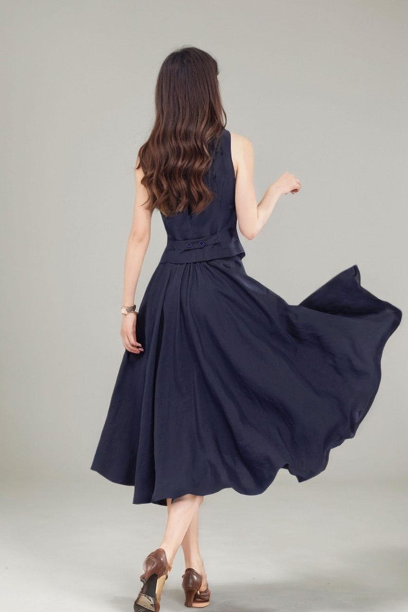 Peut inclure: Une robe bleu marine sans manches avec une jupe qui s'&eacute;vase &agrave; partir de la taille. La robe a une fermeture boutonn&eacute;e dans le dos.