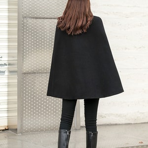 May include: A black cape with a long, flowing design. The cape is worn over black pants and black knee-high boots. The person is wearing a brown hat.