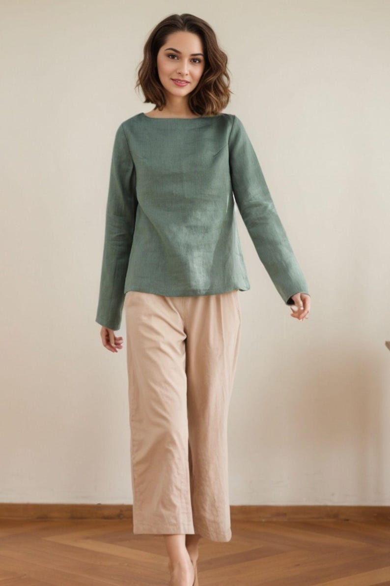 May include: A woman is wearing a sage green linen top with long sleeves and a relaxed fit. She is also wearing beige wide-leg pants.
