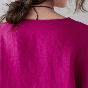 May include: A close-up of a magenta-colored top with a square neckline. The fabric appears to be linen or a similar lightweight material. The top is loose-fitting and has short sleeves. The image shows the back of the top.