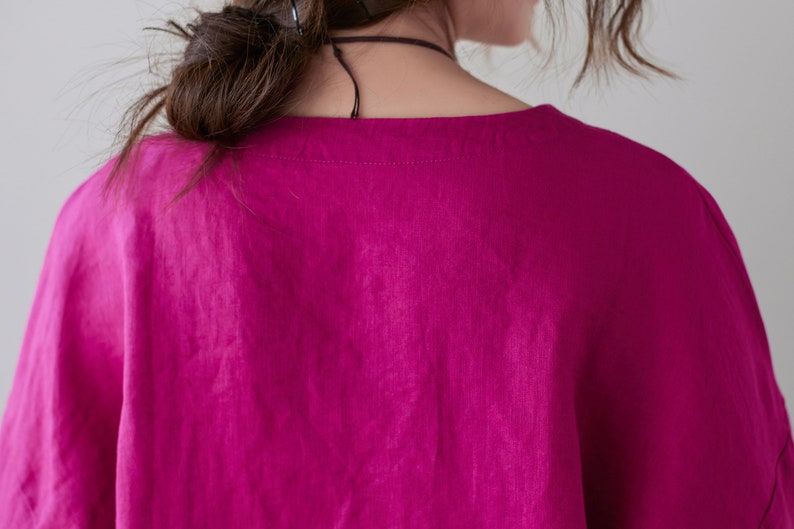 May include: A close-up of a magenta-colored top with a square neckline. The fabric appears to be linen or a similar lightweight material. The top is loose-fitting and has short sleeves. The image shows the back of the top.