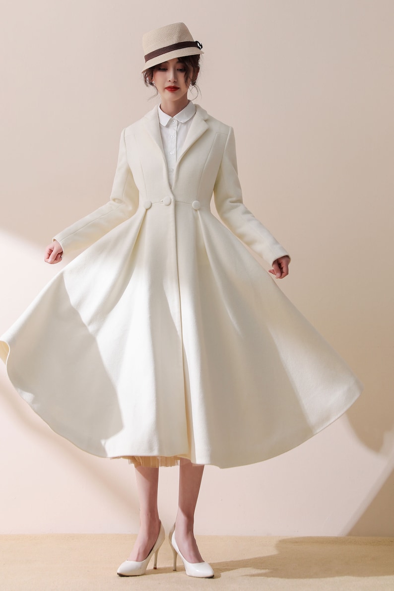 May include: A white, long-sleeved coat with a flared skirt and a single button closure. The coat is worn by a person wearing a white shirt and a straw hat.