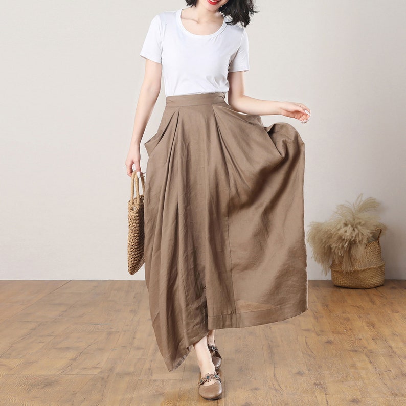 May include: A brown linen maxi skirt with a high waist and pleats. The skirt has a slightly asymmetrical hemline and is made of a lightweight, breathable fabric.