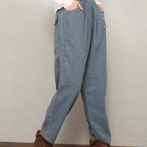 May include: Blue linen pants with a button fly and a patch pocket on the right leg. The pants have a relaxed fit and are worn with brown ankle boots.