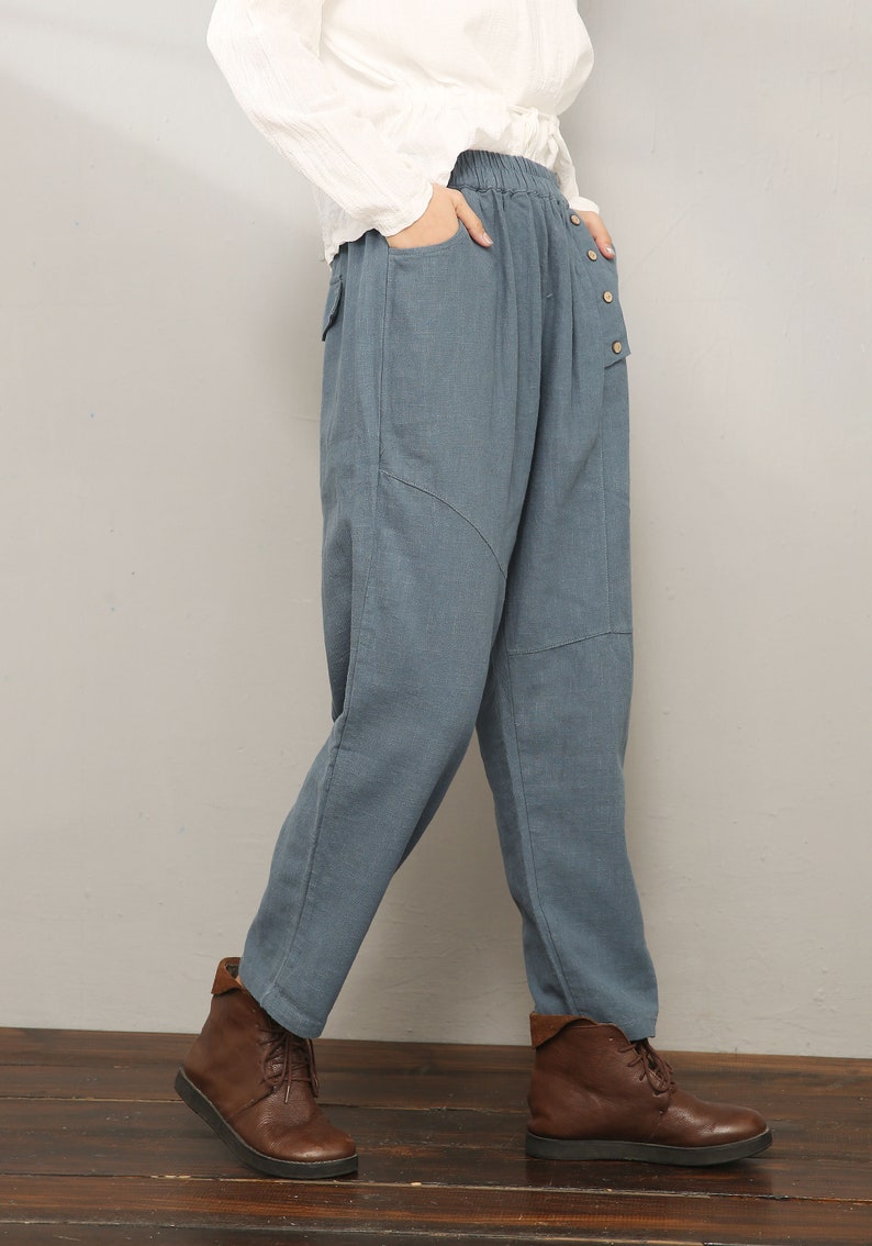 May include: Blue linen pants with a button fly and a patch pocket on the right leg. The pants have a relaxed fit and are worn with brown ankle boots.