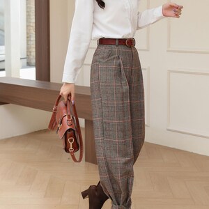 K&ouml;nnte beinhalten: Eine Person tr&auml;gt ein wei&szlig;es Hemd, eine braune karierte Hose und braune Lederstiefel. Ein brauner Lederg&uuml;rtel und eine Handtasche vervollst&auml;ndigen das Outfit. Die Hose hat eine plissierte Vorderseite und ist an den Kn&ouml;cheln umgeschlagen.