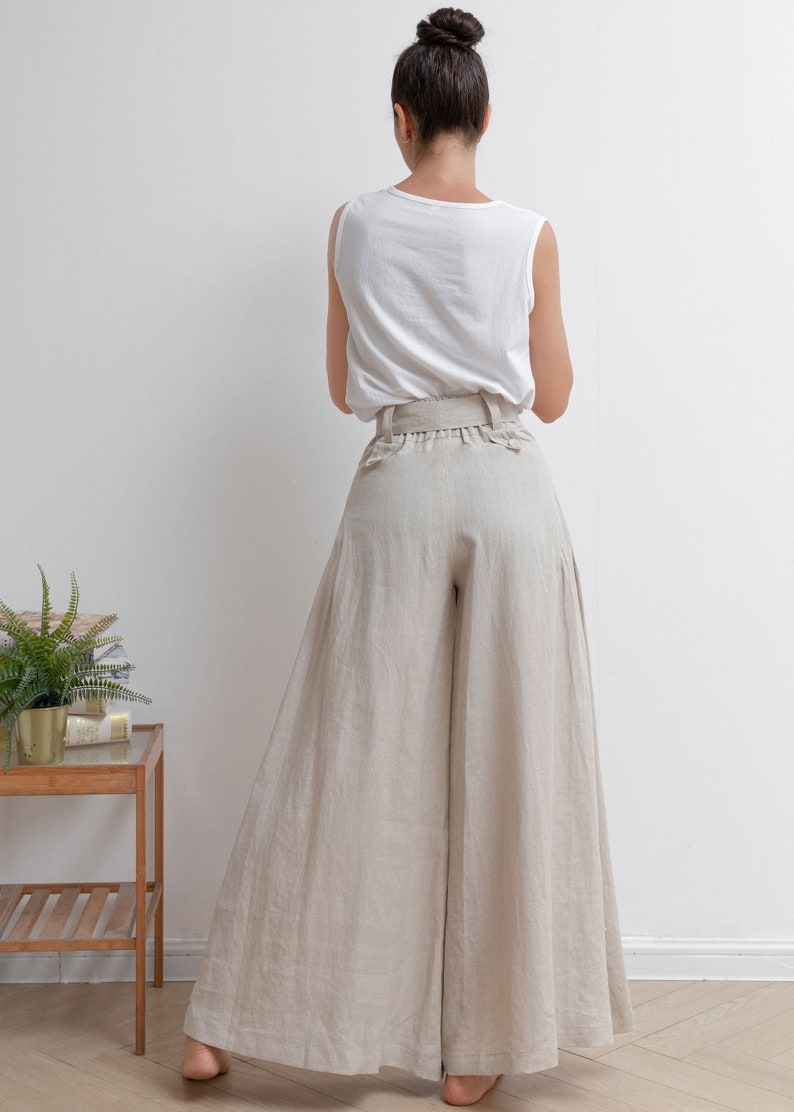 May include: A woman wearing a white sleeveless top and wide-legged, light beige linen pants with a wide belt.