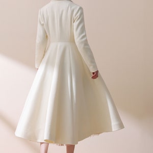 May include: A white long-sleeved coat with a flared skirt and a high collar. The coat is made of a soft, luxurious fabric and has a classic, elegant design.