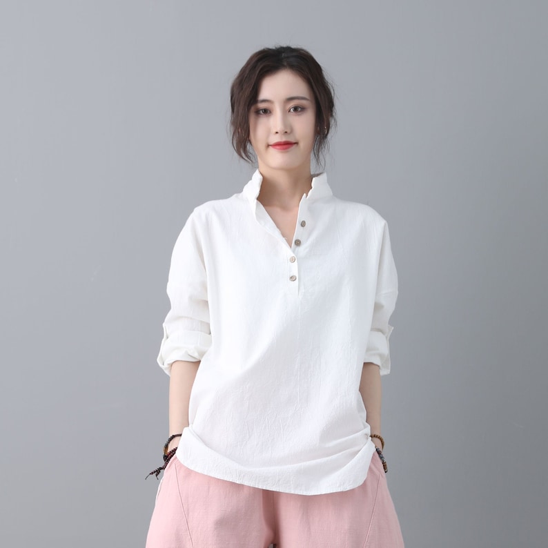 May include: A white long-sleeved button-down shirt with a collar and a relaxed fit. The shirt is made of a lightweight fabric and has a slightly textured surface.