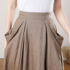 May include: A brown linen skirt with large pockets on the sides. The skirt has a high waist and a flowing silhouette.