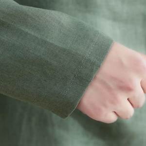 May include: Close-up of a green linen shirt sleeve with a stitched seam. The fabric is soft and textured.