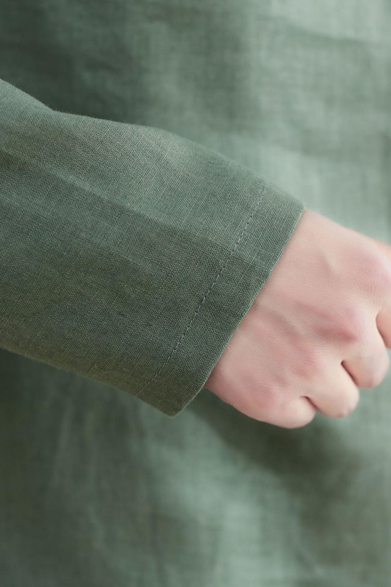 May include: Close-up of a green linen shirt sleeve with a stitched seam. The fabric is soft and textured.