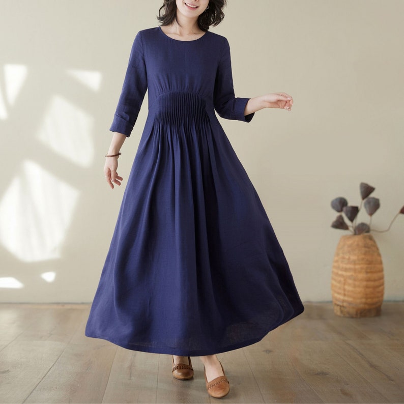 May include: A navy blue linen dress with a round neckline and 3/4 sleeves. The dress has a pleated skirt and a fitted bodice.
