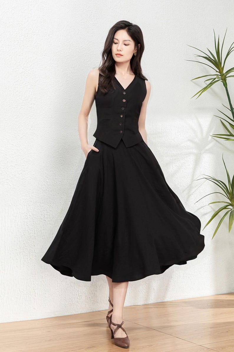 Peut inclure: Un gilet noir sans manches avec un col en V et une fermeture &agrave; boutons, port&eacute; avec une jupe noire &eacute;vas&eacute;e. La tenue est port&eacute;e par une femme aux cheveux longs et fonc&eacute;s et des chaussures brunes.