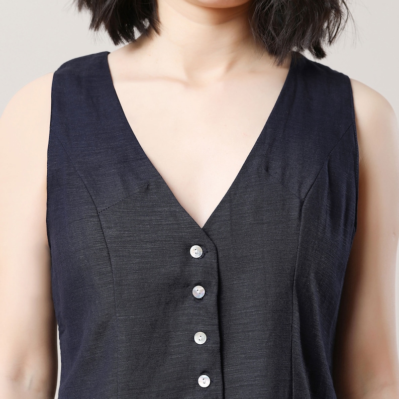 May include: A sleeveless black dress with a deep V-neckline and a row of silver buttons down the front.