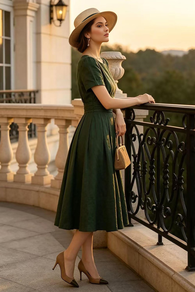 May include: A dark green midi dress with short sleeves and a fitted waist, paired with a tan straw hat, a small tan handbag with a metal frame, and tan high-heeled pumps featuring black pointed toes, worn in a setting with a stone balcony railing.