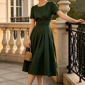 May include: A dark green midi dress with short sleeves, a round neckline, and a pleated skirt with a cinched waist. The outfit includes a tan straw hat, a small brown structured handbag, and two-tone tan and black pointed-toe high heel pumps.