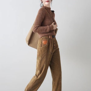K&ouml;nnte beinhalten: Eine Frau tr&auml;gt einen braunen Rollkragenpullover und eine braune Cordhose mit einem braunen Lederg&uuml;rtel und einer braunen Leder-Patch-Tasche. Sie tr&auml;gt wei&szlig;e Turnschuhe und tr&auml;gt eine braune Papiert&uuml;te.