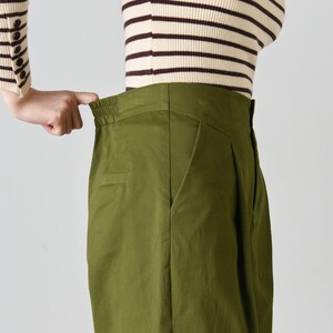 Op de afbeelding: Groene broek met hoge taille, wijde pijpen en een bruin-wit gestreept shirt.