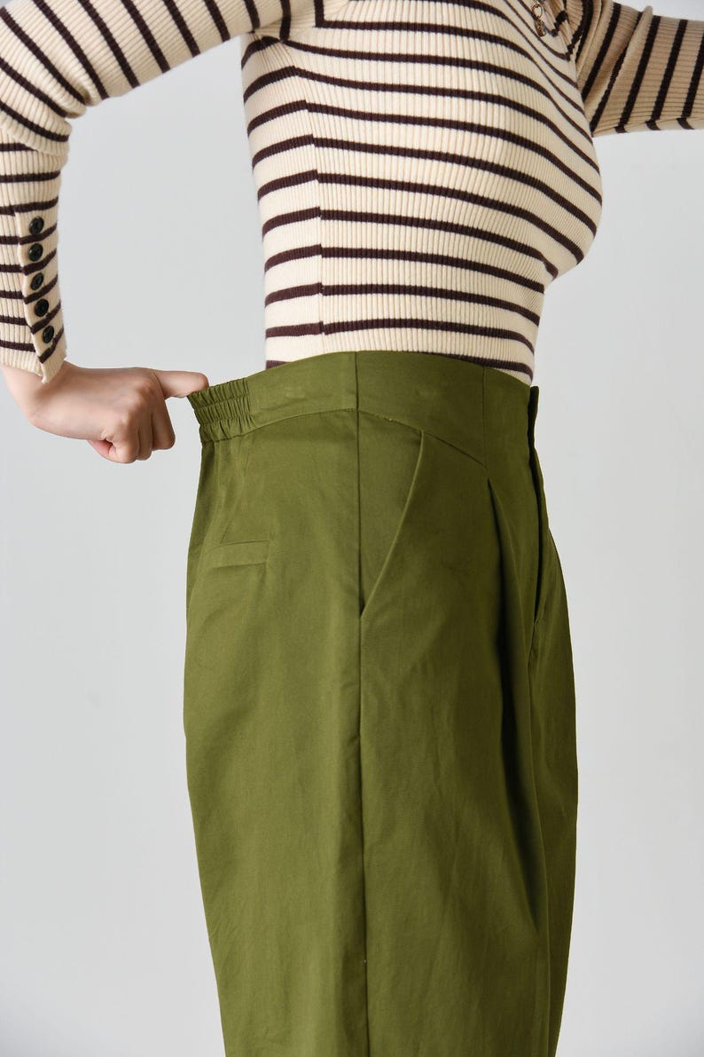 Op de afbeelding: Groene broek met hoge taille, wijde pijpen en een bruin-wit gestreept shirt.