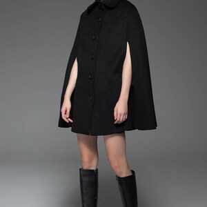 May include: A black wool cape with a button-up front and long sleeves. The cape is knee-length and has a wide, flowing silhouette.