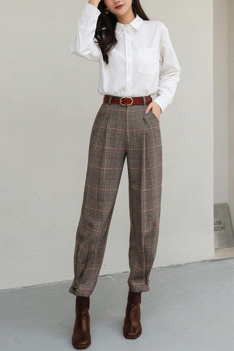 K&ouml;nnte beinhalten: Ein wei&szlig;es Hemd mit Knopfleiste, eine braune karierte Hose und ein brauner Lederg&uuml;rtel. Die Hose hat eine Faltenfront und ist an den Kn&ouml;cheln geb&uuml;ndelt. Braune Lederstiefel vervollst&auml;ndigen das Outfit.