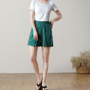 May include: A person wearing a white short-sleeved t-shirt and emerald green shorts with pockets. The person is also wearing black platform sandals. The outfit is casual and comfortable.