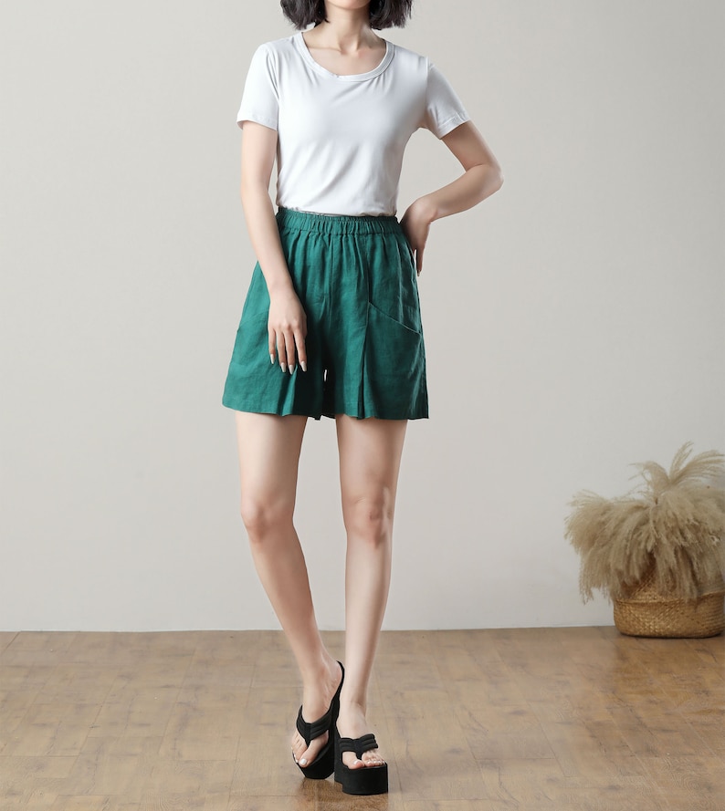 May include: A person wearing a white short-sleeved t-shirt and emerald green shorts with pockets. The person is also wearing black platform sandals. The outfit is casual and comfortable.